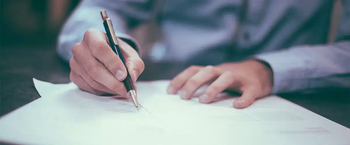 A hand signing a document with a pen