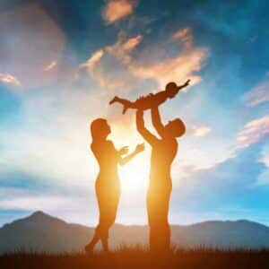 A happy couple holding their child high in sunset after getting approval for their e2 visa business plan for franchise